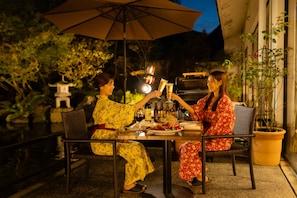 Two people seated at an outdoor table with an umbrella, surrounded by greenery and a stone lantern. - Hotel Hoho "A hotel overlooking the Echigo Plain and the Yahiko mountain range" (Niigata)