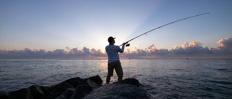 A person fishing at a rocky shoreline with a clear view of the ocean and sky.