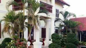 A colonial-style building with a balcony, palm trees, and a patio with benches. - Phonepraseuth Guesthouse (Luang Prabang)