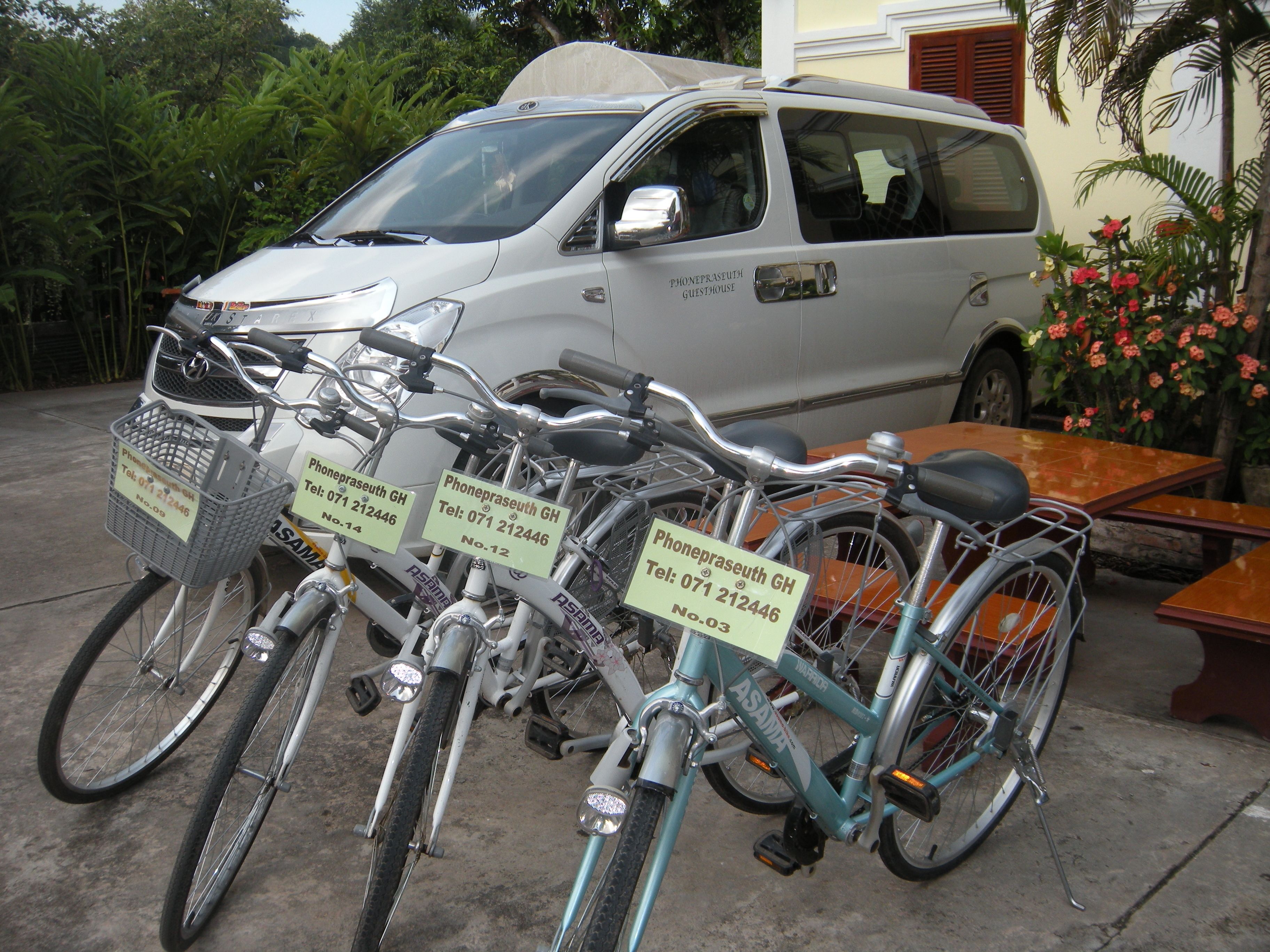 Een rij fietsen met bevestigde telefoonnummers en een bestelwagen op de achtergrond.