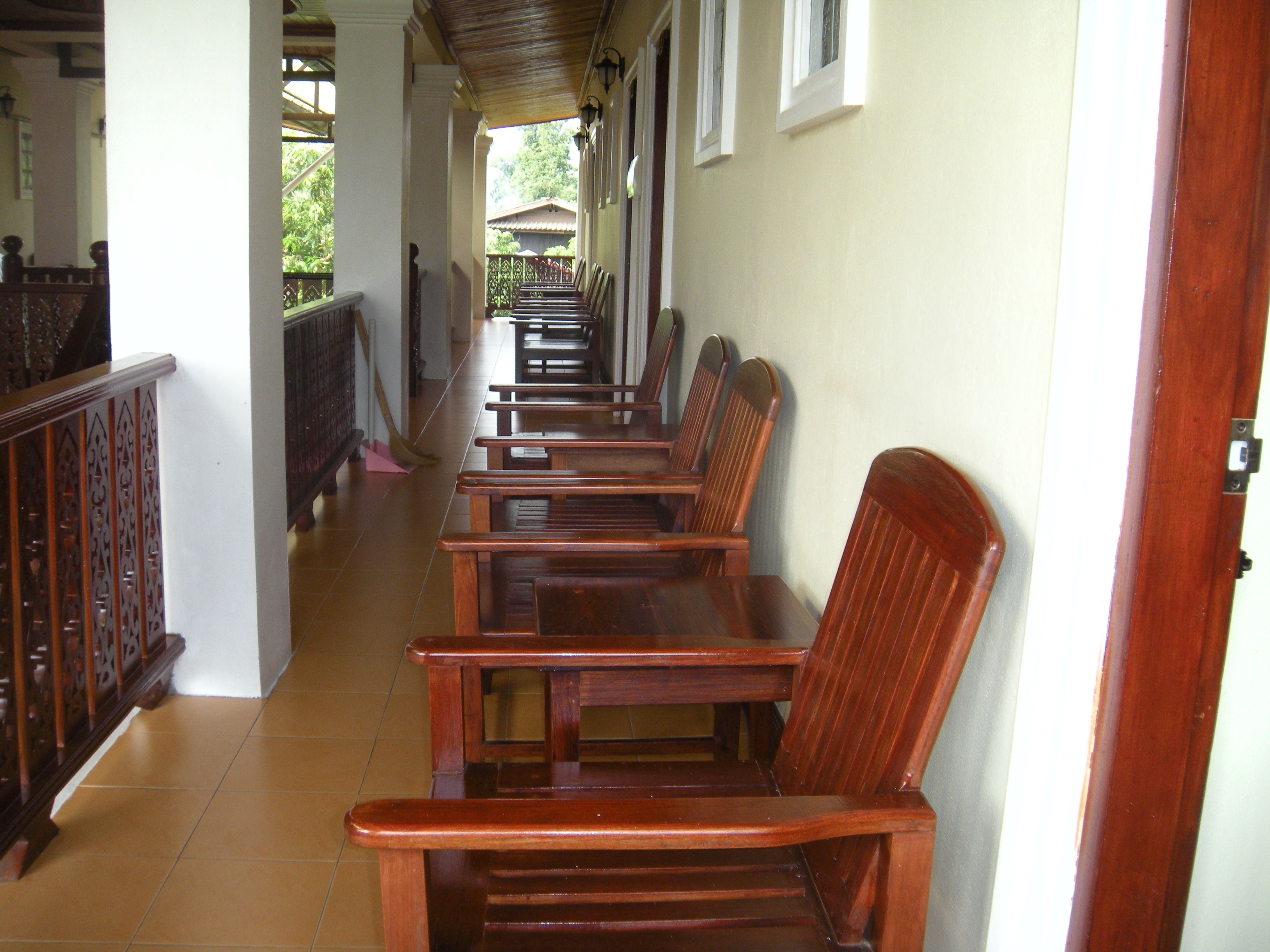 A corridor with wooden benches and a tiled floor, leading to a covered area with a railing.