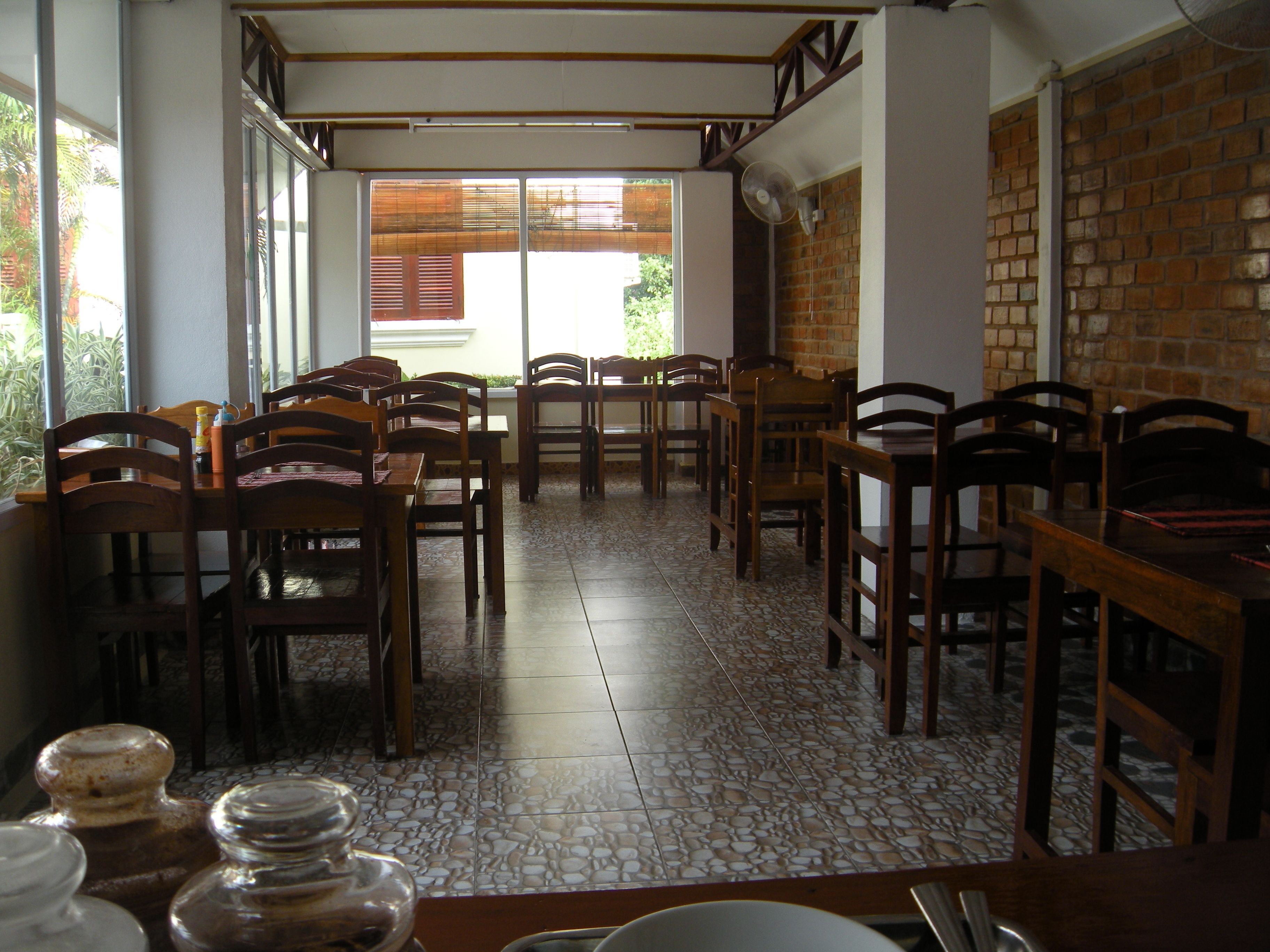 Un espace repas avec des tables et des chaises en bois, un sol carrelé et un mur en briques.