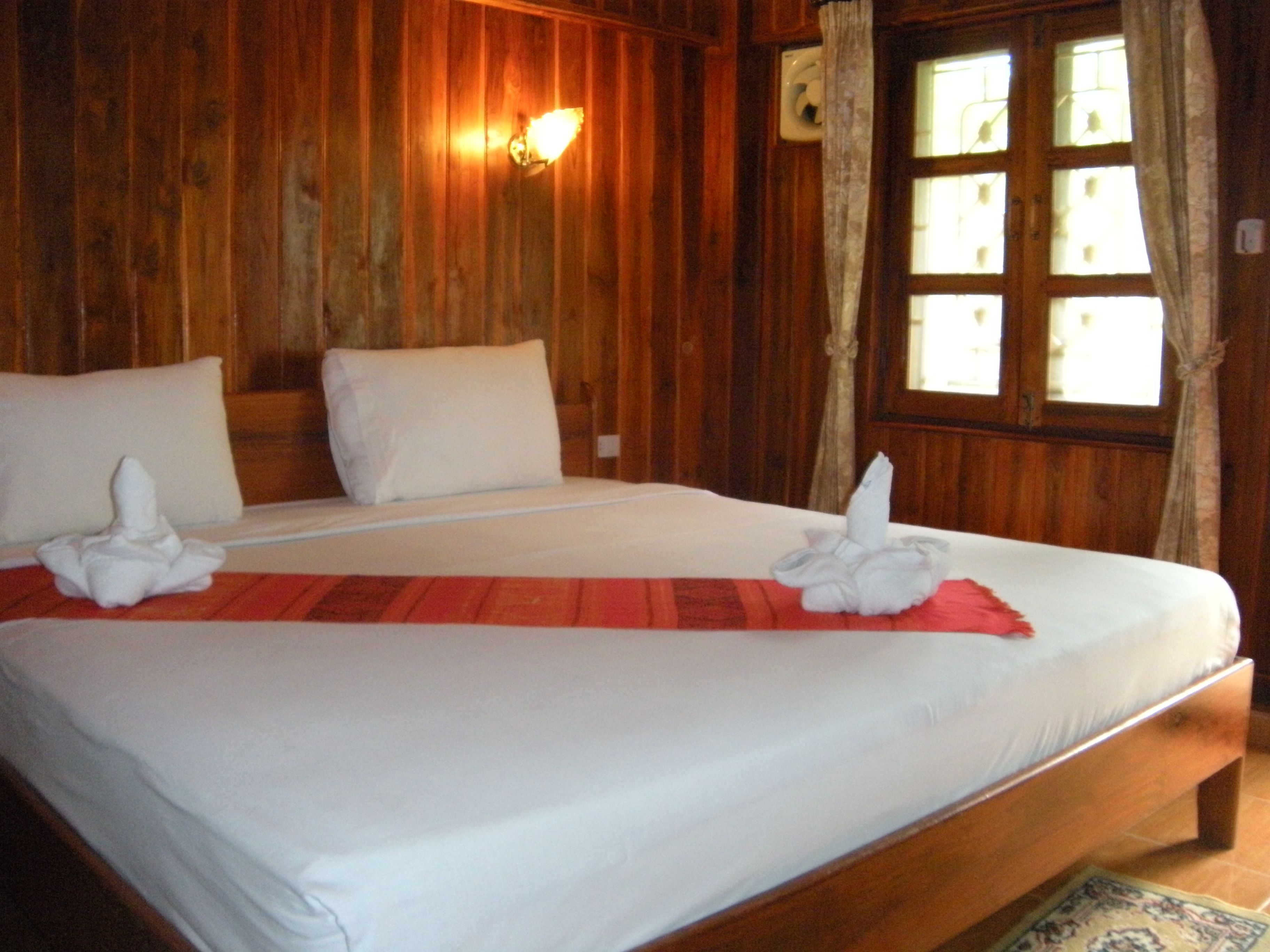 A wooden room with a bed, pillows, a wall-mounted light, and a window with curtains.