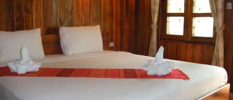A wooden room with a bed, pillows, a wall-mounted light, and a window with curtains.
