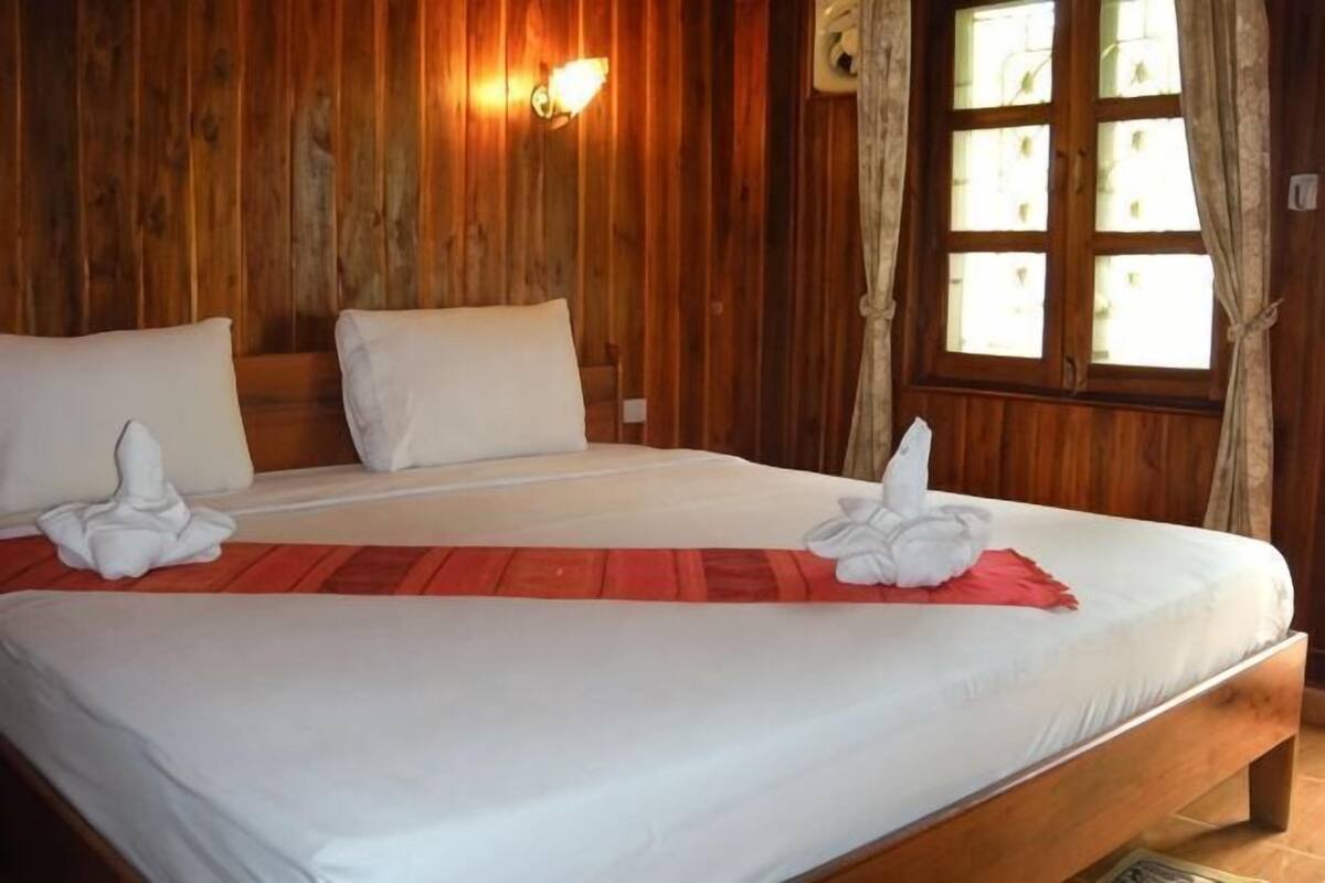 Ein ordentlich bezogenes Bett mit weißen Leinen und Handtüchern, Holzwände und einem Fenster mit Vorhängen.