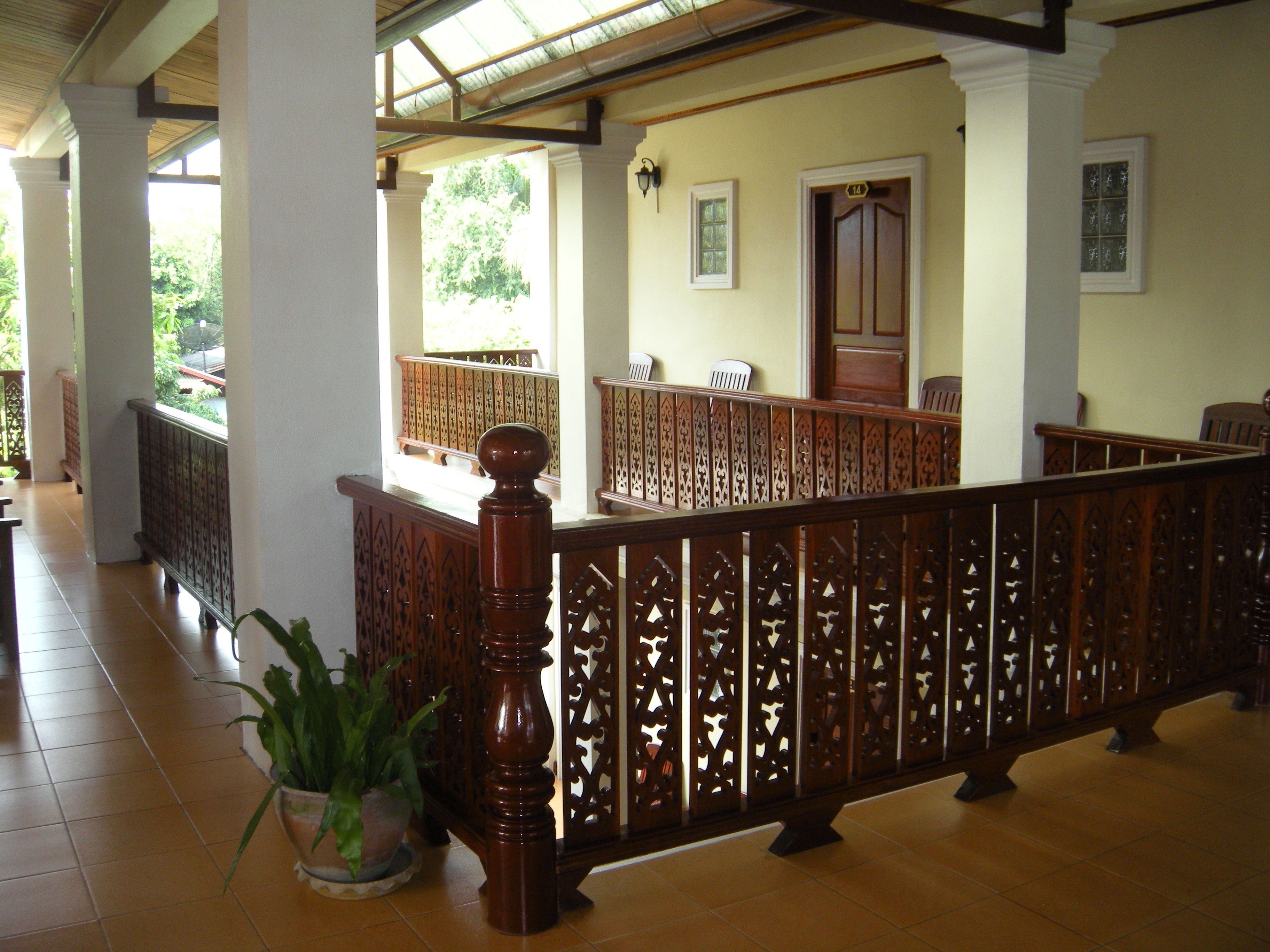 A covered corridor with a wooden railing, potted plants, and a tiled floor.