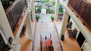 A spacious atrium with a central wooden table and chairs, surrounded by potted plants and a view of a garden. - Phonepraseuth Guesthouse (Luang Prabang)