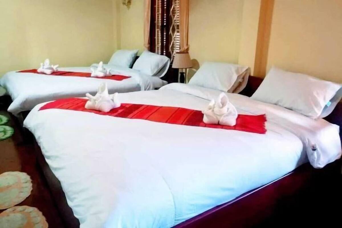 Ein Hotelzimmer mit zwei Betten, jeweils mit weißer Bettwäsche und roten Akzenten, sowie einer Lampe auf dem Nachttisch.