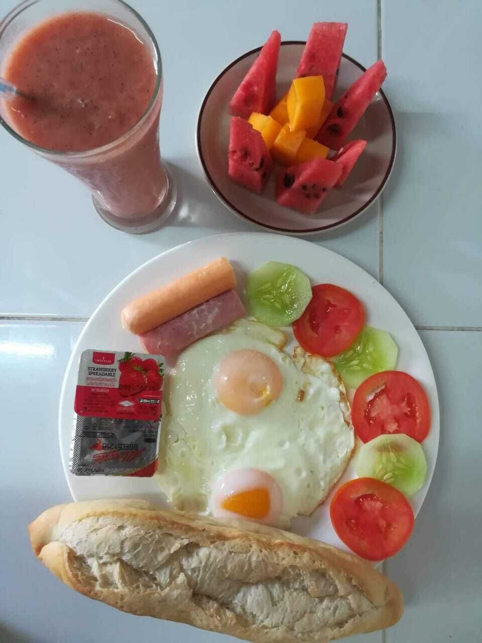 A breakfast plate with eggs, sausage, tomatoes, cucumbers, and bread.