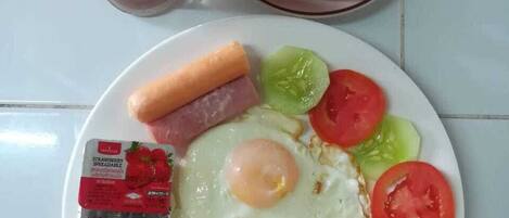 A breakfast plate with eggs, sausage, tomatoes, cucumbers, and bread.