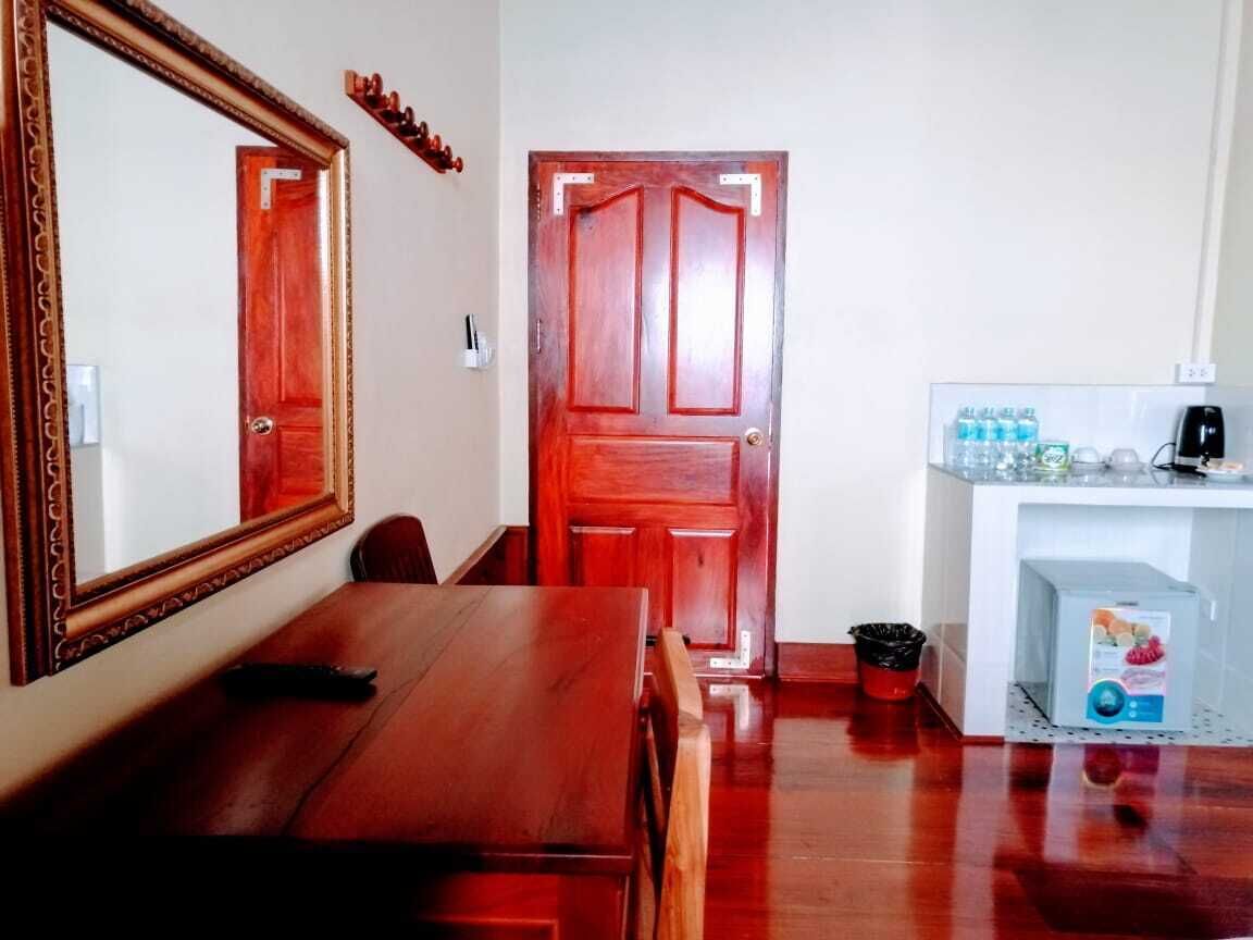Una mesa de comedor de madera con sillas, un espejo, una puerta de madera y una pequeña zona de kitchenette con una cafetera y recipientes de almacenamiento.