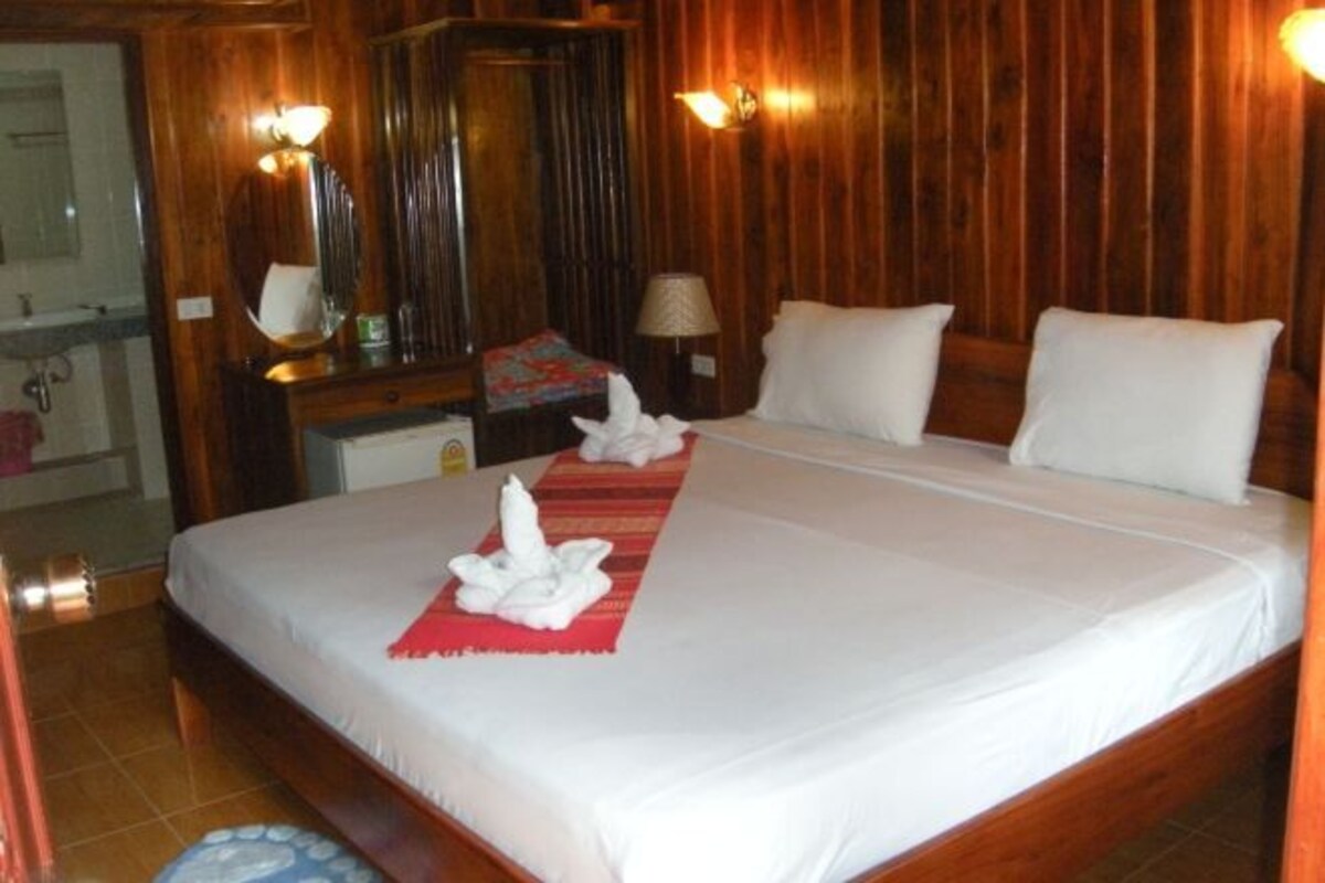 A hotel room with a wooden paneled wall, a bed with white linens, a red throw, and a mirror above the bed.