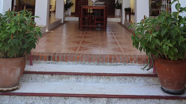A covered entrance with a staircase leading to a second floor, flanked by columns and potted plants. - Phonepraseuth Guesthouse (Luang Prabang)