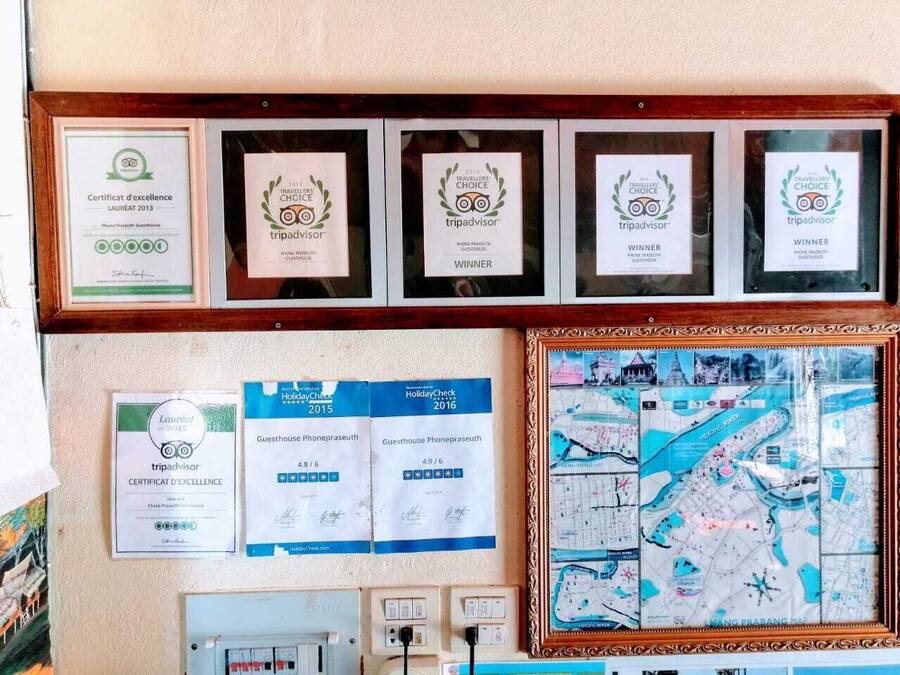 Framed awards and certificates on a wall, including TripAdvisor and HolidayCheck recognitions, and a framed map.