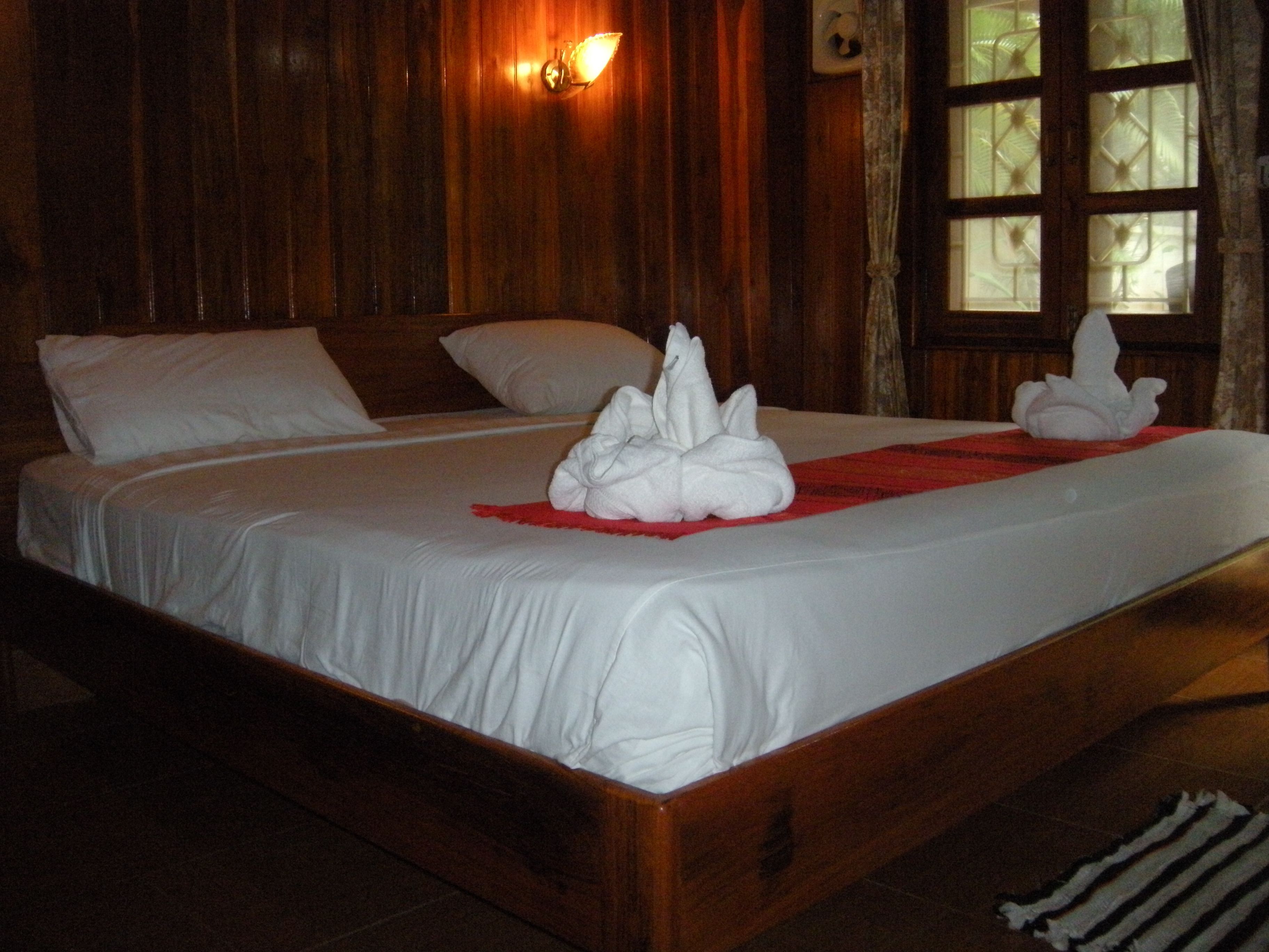 A wooden bed with white linens and two white towels arranged on the bed.