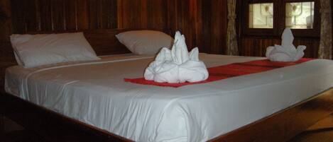 A wooden bed with white linens and two white towels arranged on the bed.