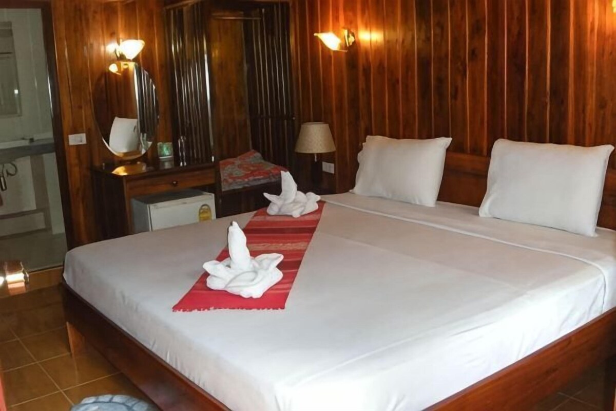 Una habitación de hotel con una cama grande, paneles de madera, un escritorio con lámpara y un espejo.