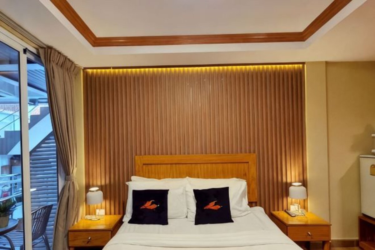 A hotel room with a large bed, two bedside tables, a headboard, and a view of the outside.