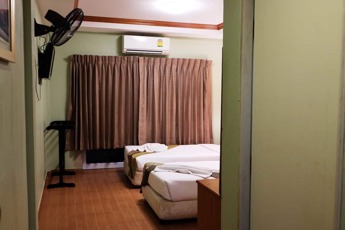 A hotel room with two beds, a standing fan, an air conditioner, and a curtain.