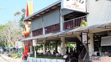 Un hotel con restaurante en la planta baja, mesas al aire libre y una escalera que sube al segundo piso.