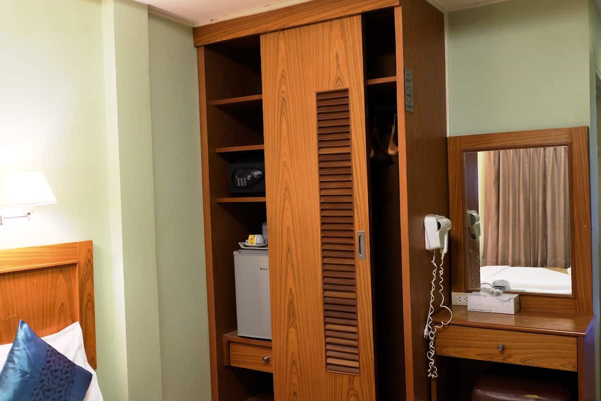 A wooden wardrobe with a mirror, a small refrigerator, and a bedside table with a lamp.