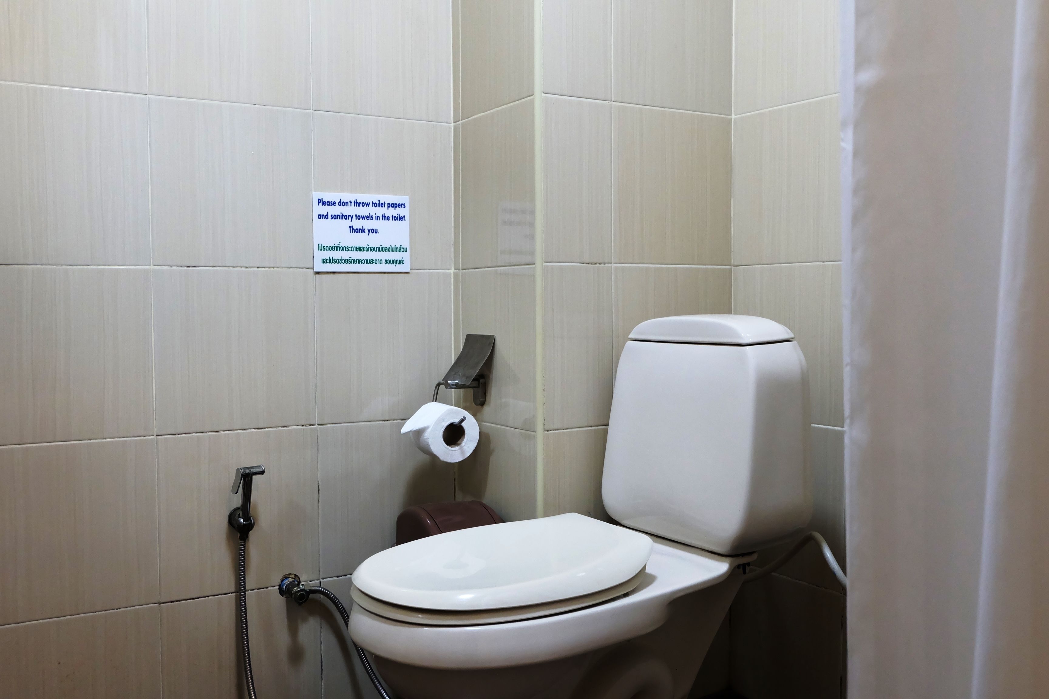 A bathroom with a toilet, a paper towel dispenser, and a sign instructing to throw toilet papers and sanitary towels in the toilet.