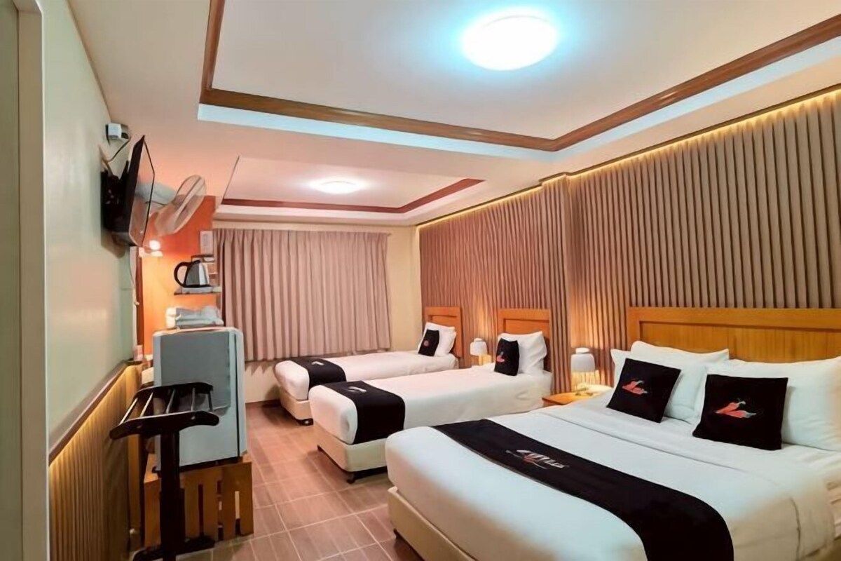 A hotel room with two beds, a desk, a TV, and a fan.