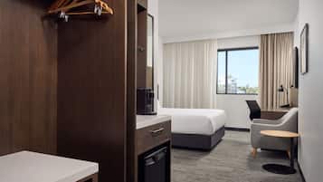A hotel room with a bed, a desk, a chair, a small table, a wardrobe, and a window with curtains.
