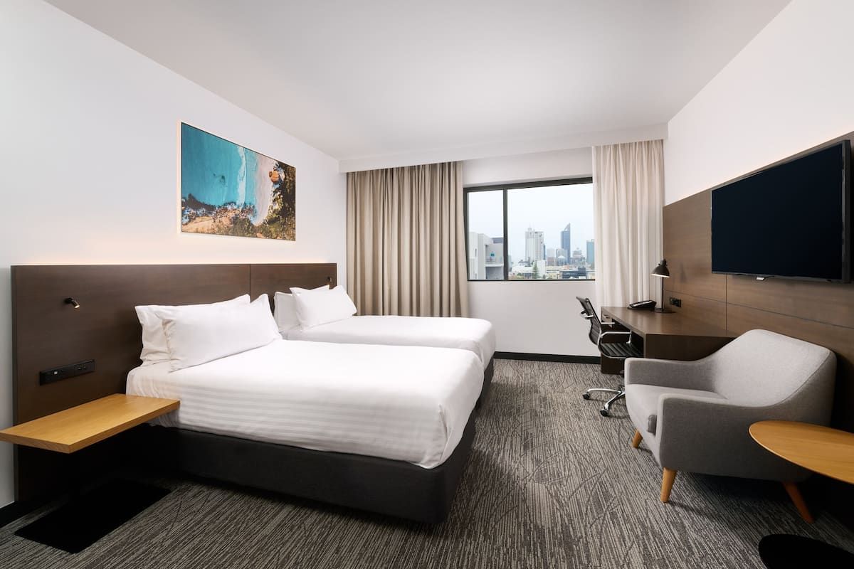 A hotel room with a large bed, a desk, a chair, a TV, and a city view.