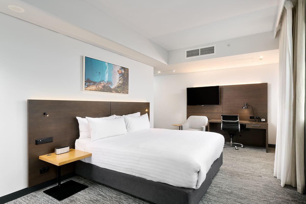 A hotel room with a large bed, a desk, a chair, a flat-screen TV, and a painting on the wall.