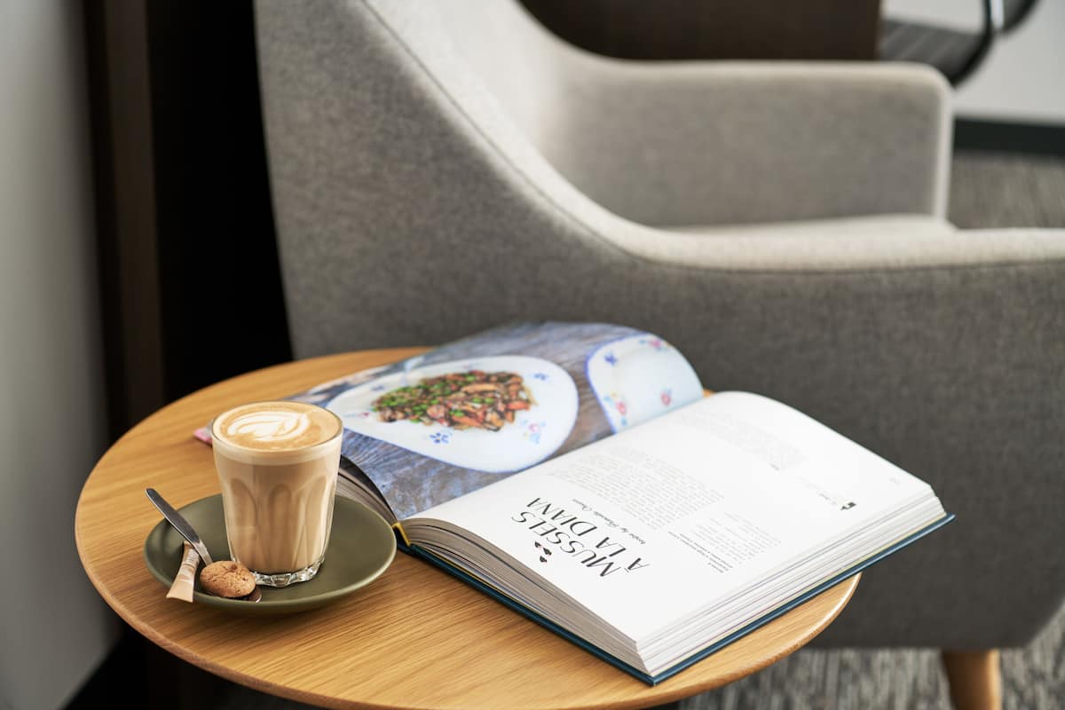 A table with a book, a cup of coffee, and a cookie.