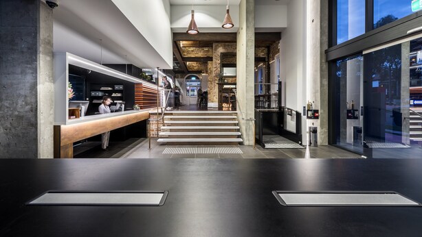 Un interior moderno con un mostrador de recepción, una escalera y ventanas amplias.