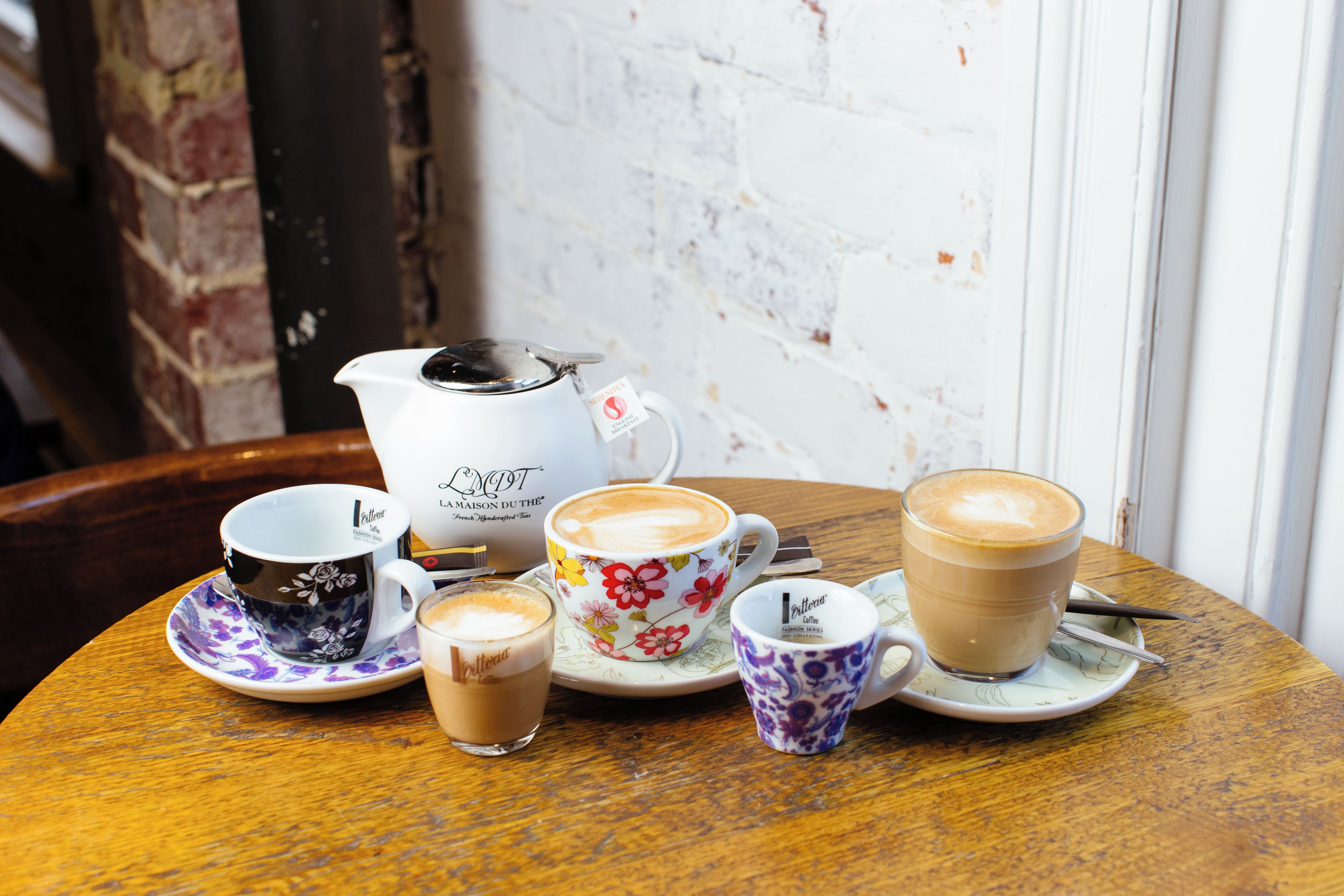 A table with various cups of coffee and a teapot, suggesting a coffee service setting.