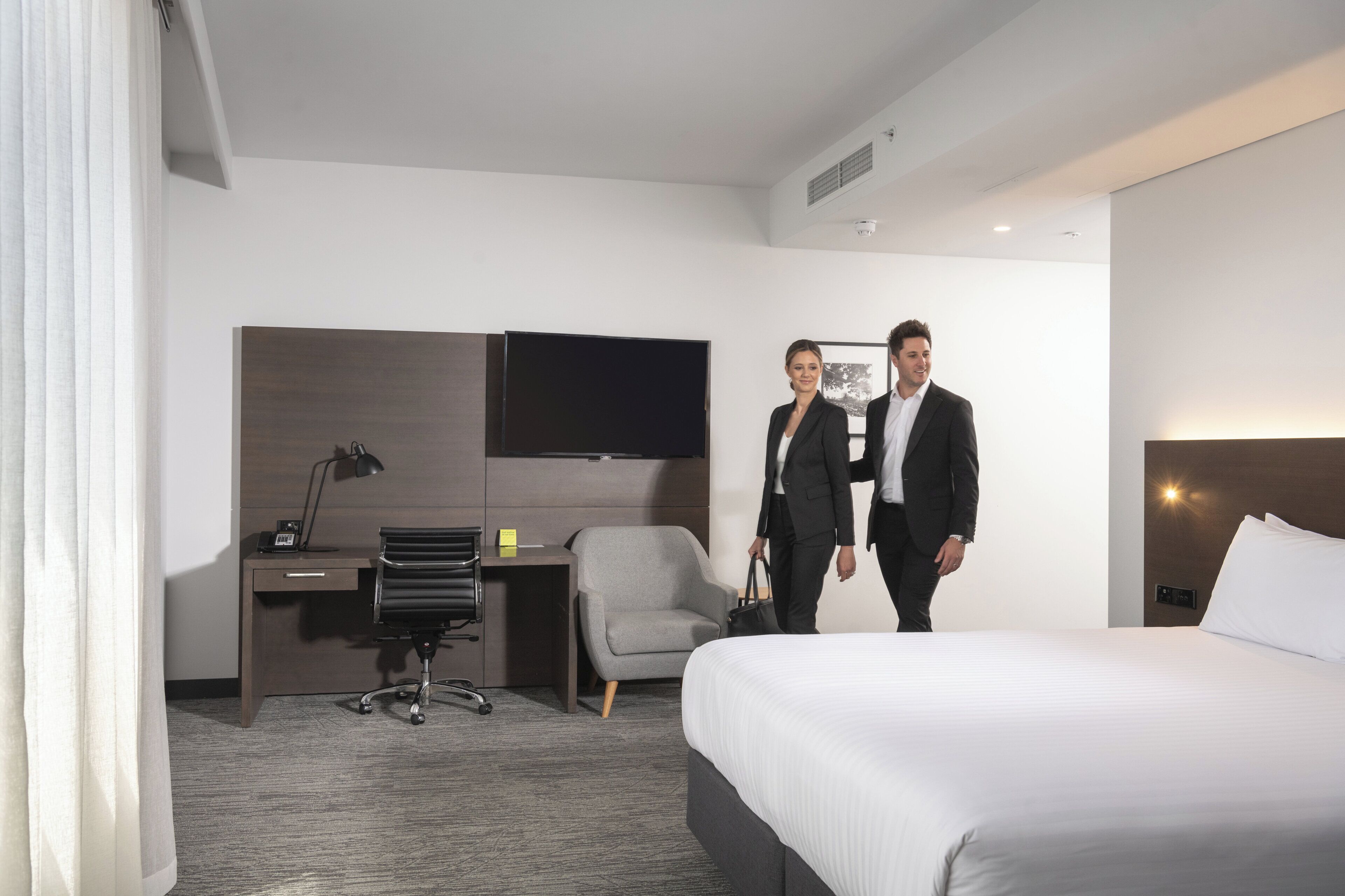 A hotel room with a bed, a desk with a chair, a flat-screen TV, and a small table.