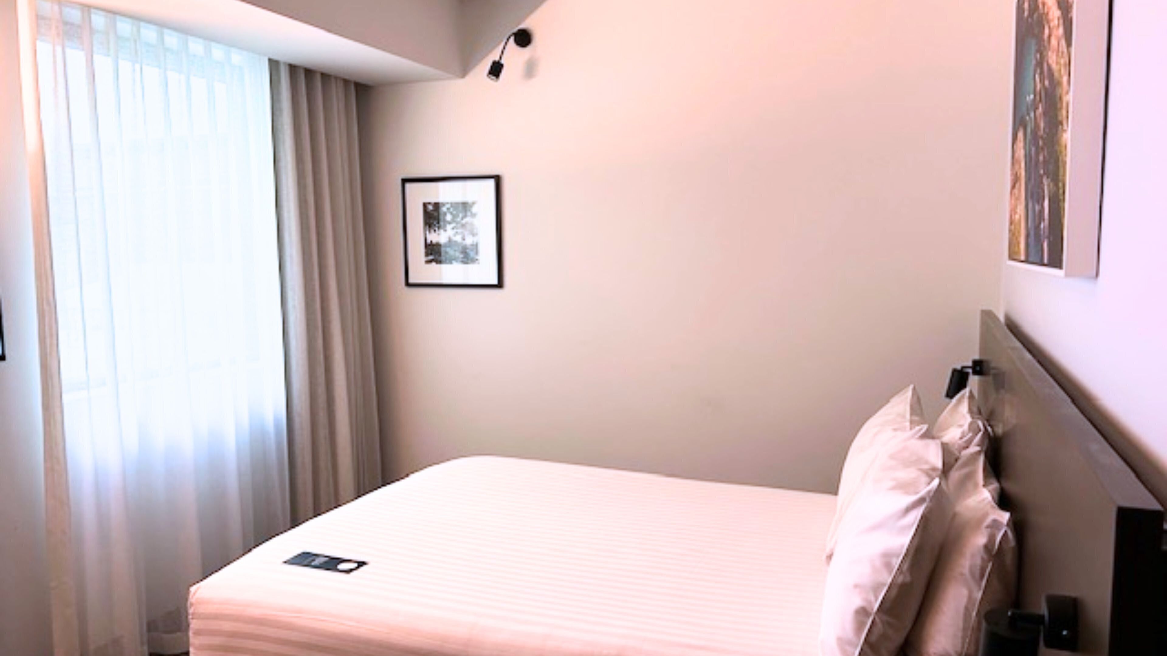 A hotel room with a bed, a bedside table, a lamp, and a window with curtains.
