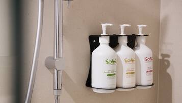Un baño con ducha y tres botellas de productos para el cabello Soak sobre un soporte negro.