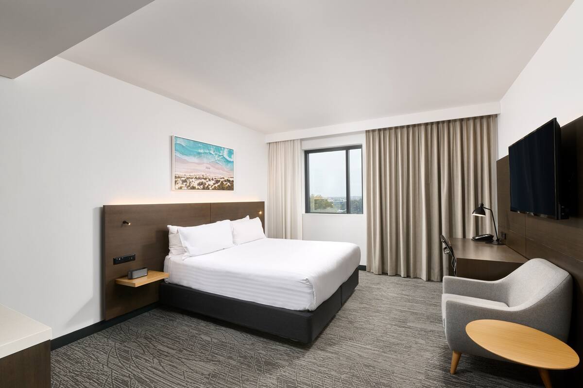 A modern hotel room with a large bed, a desk, a chair, and a TV.