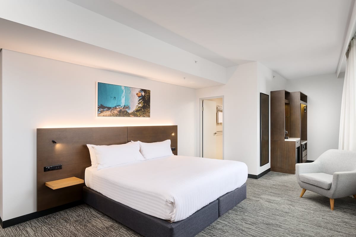 A modern hotel room with a large bed, a nightstand, a desk, a chair, and a painting on the wall.
