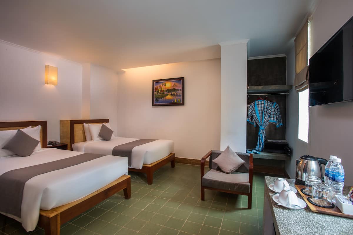 A hotel room with two beds, a chair, a painting, a TV, and a kitchenette.