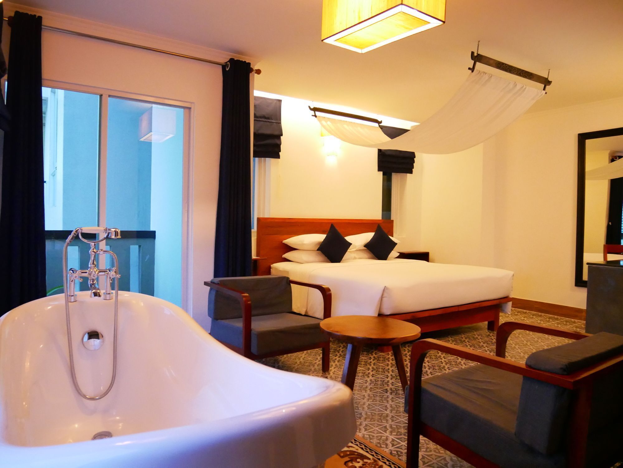 A hotel room with a large bathtub, a bed with pillows, a small round table, and a chair.