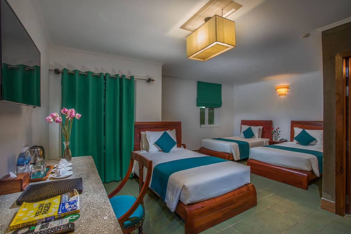 A hotel room with three wooden beds, a desk with a chair, a mirror, and a green curtain.