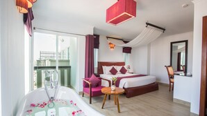 A modern hotel room with a large bathtub, a bed with a wooden headboard, a small table with a plant, and a balcony with a view. - V Hotel Phnom Penh (Phnom Penh)