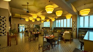 A spacious restaurant with multiple dining tables and chairs, large windows, and hanging pendant lights. - V Hotel Phnom Penh (Phnom Penh)