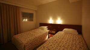 A hotel room with two beds, a nightstand, a lamp, and a window with curtains.