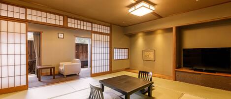 A traditional Japanese-style room with tatami flooring, a low table with cushions, a television, and sliding doors.