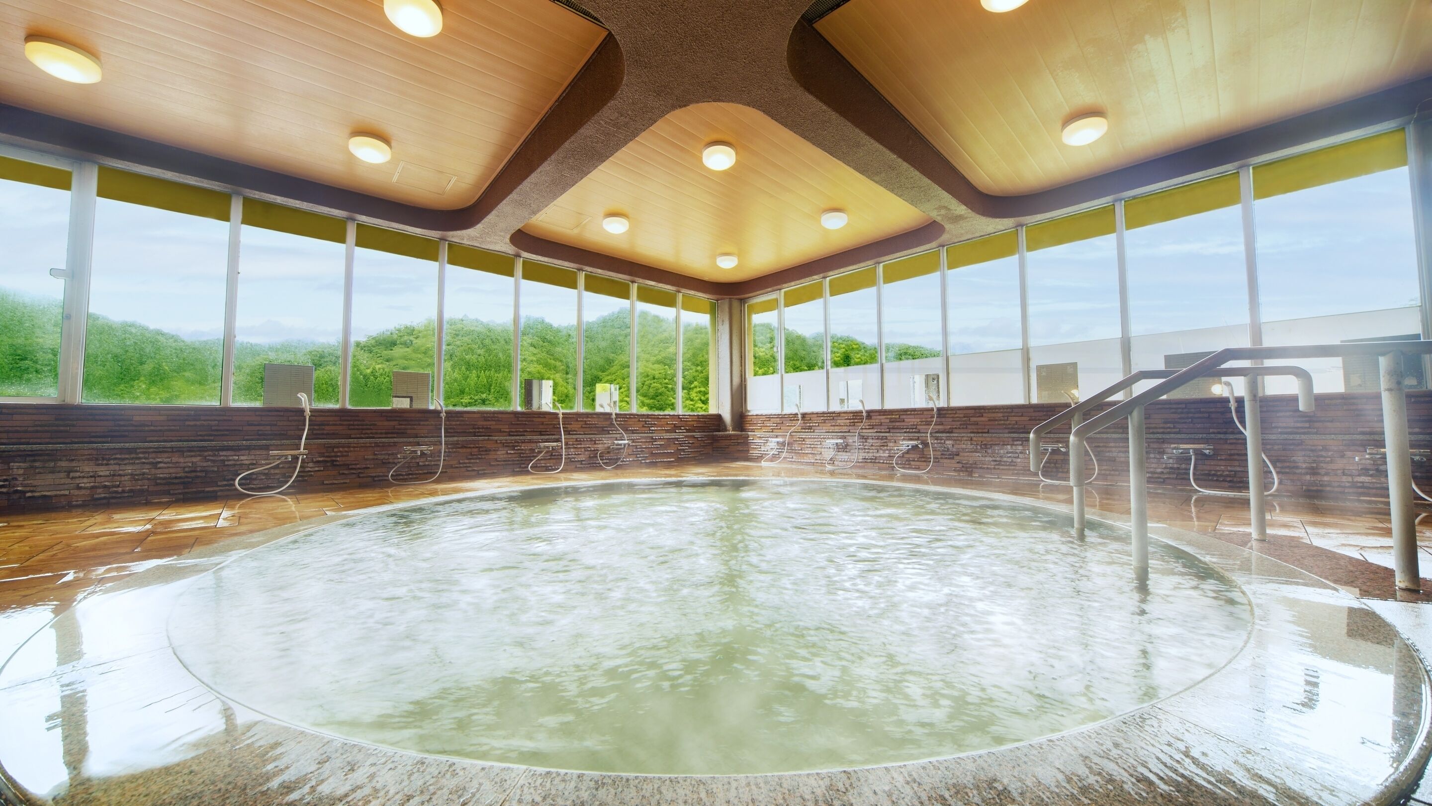 A large indoor pool with a wooden ceiling, large windows, and a brick wall.