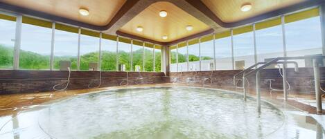 A large indoor pool with a wooden ceiling, large windows, and a brick wall.
