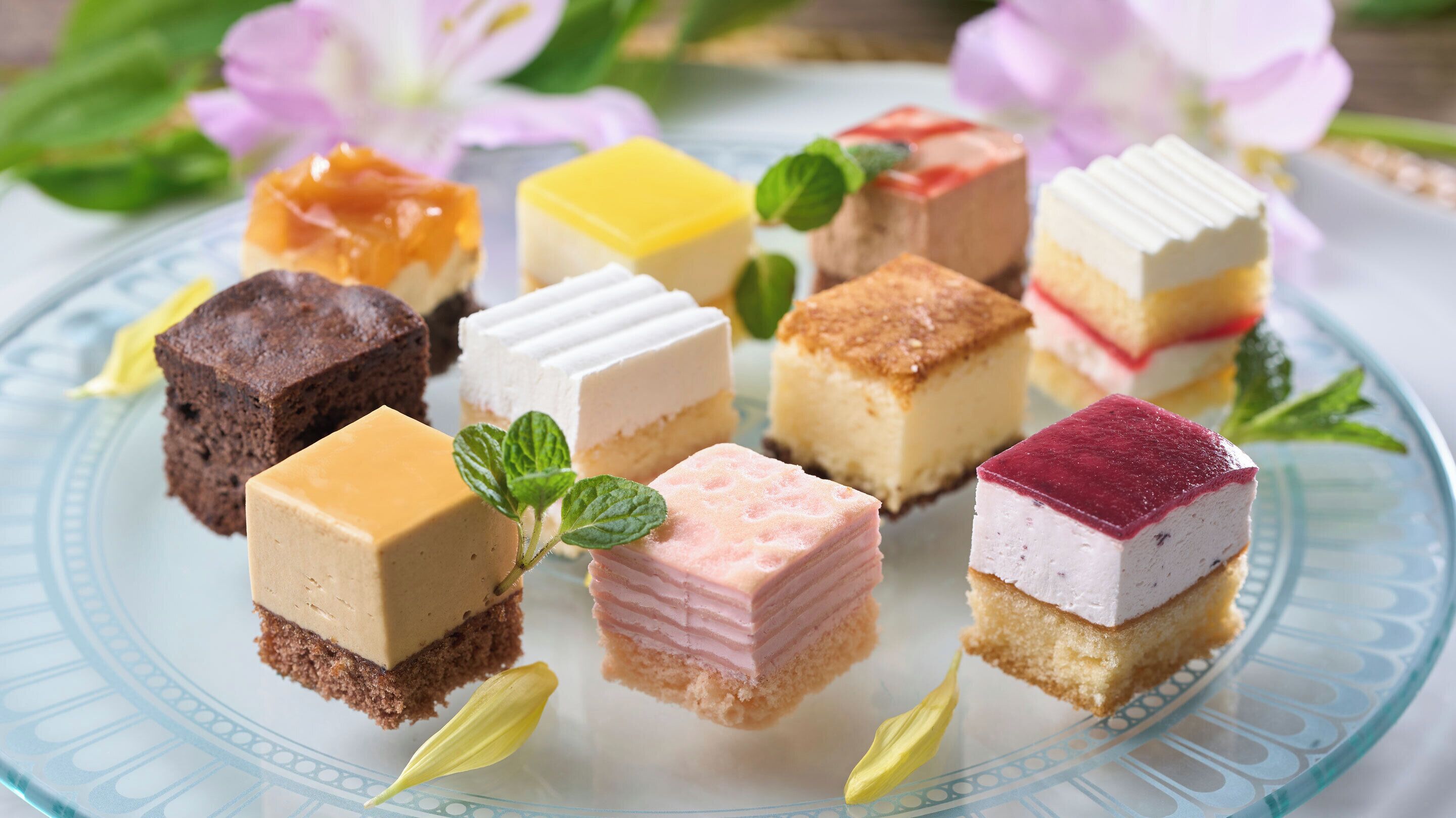 A variety of square desserts on a glass plate.
