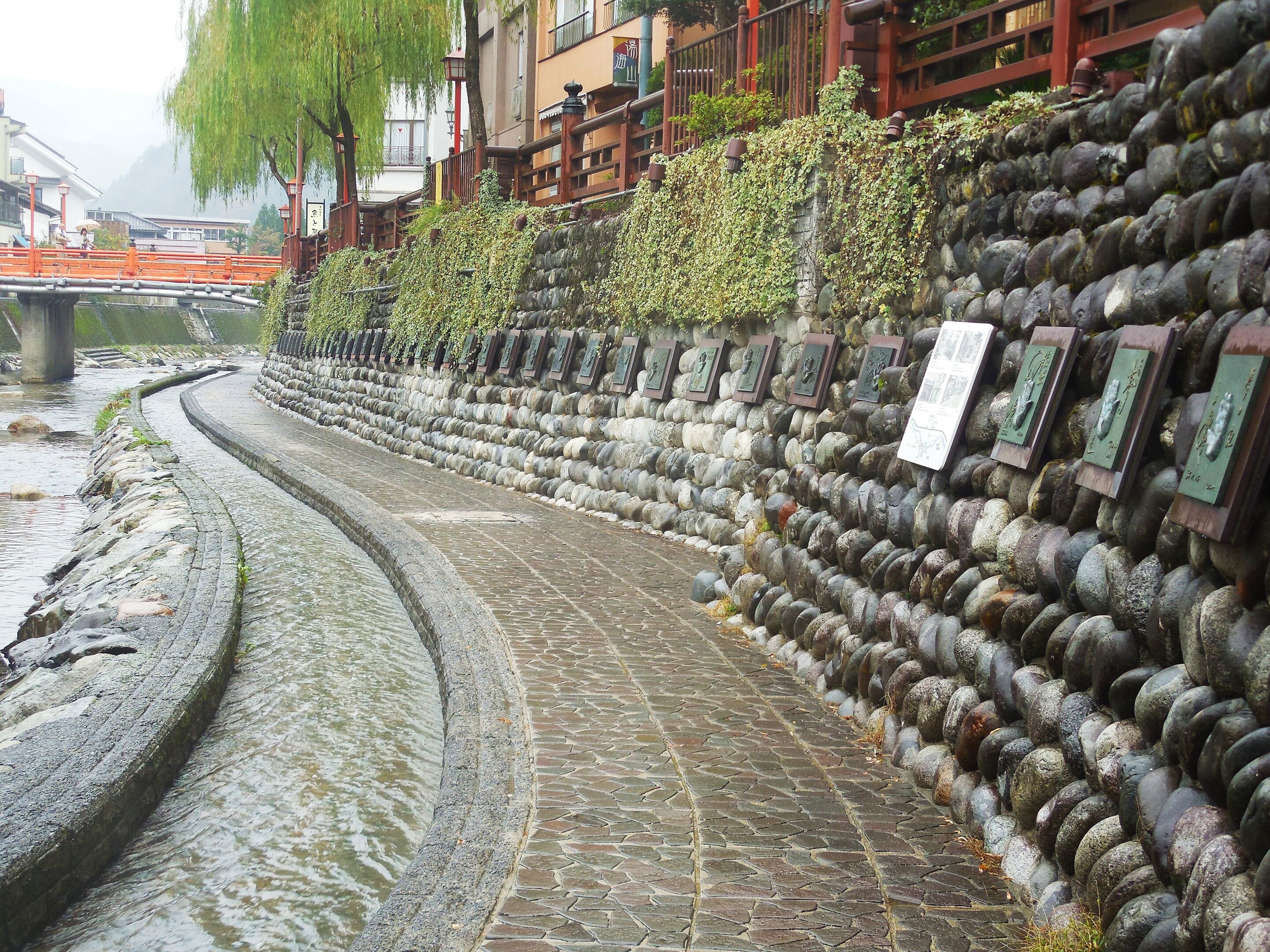 A stone pathway beside a river with a stone wall featuring plaques.