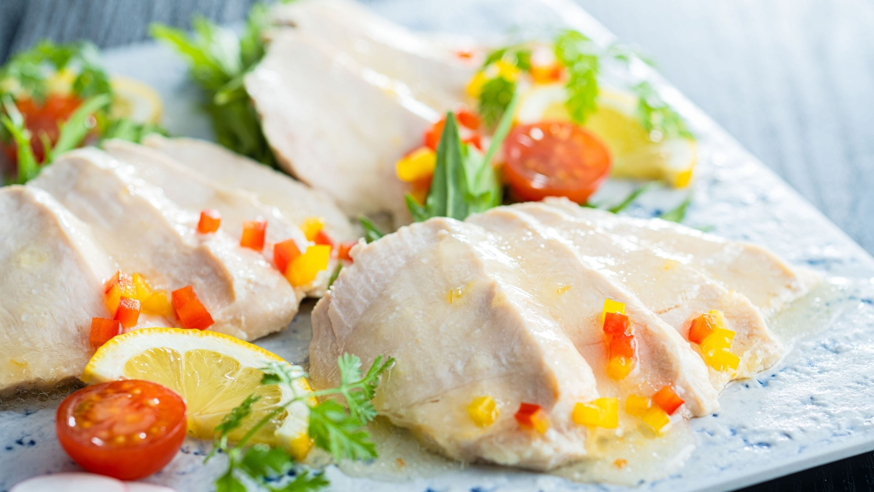 Une assiette de fines tranches de poulet, accompagnées de légumes coupés en dés et de rondelles de citron.